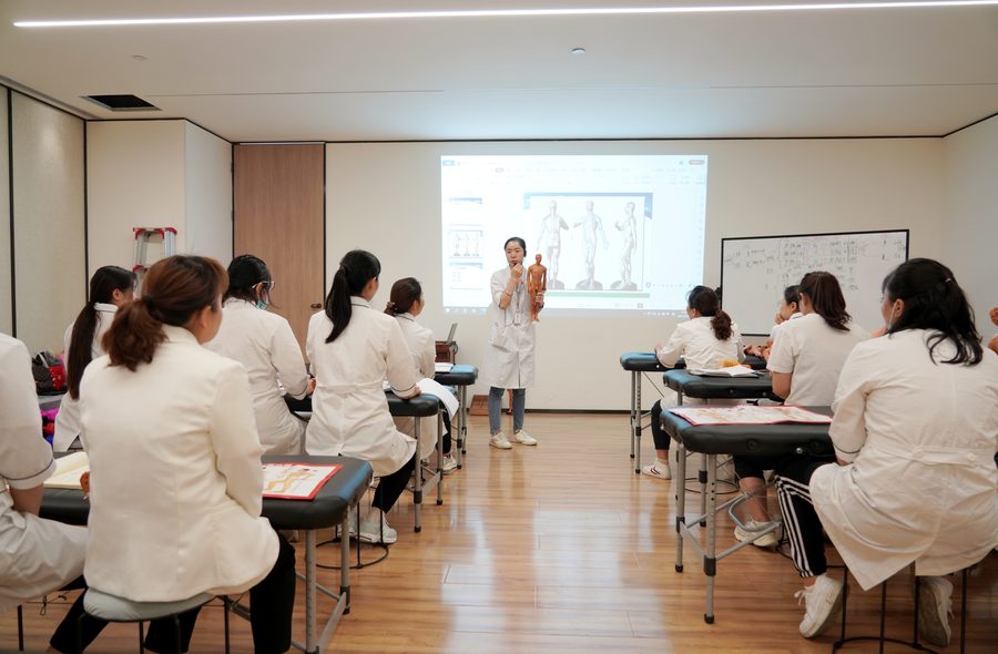 教师在投影幕前讲解经络知识，学员围坐听讲